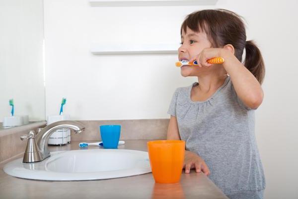 Little girl brushing her teeth with orange toothbrush and cup